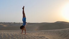 日落时分，一名女子在阿曼沙漠的沙丘上倒立，展现出平衡与宁静