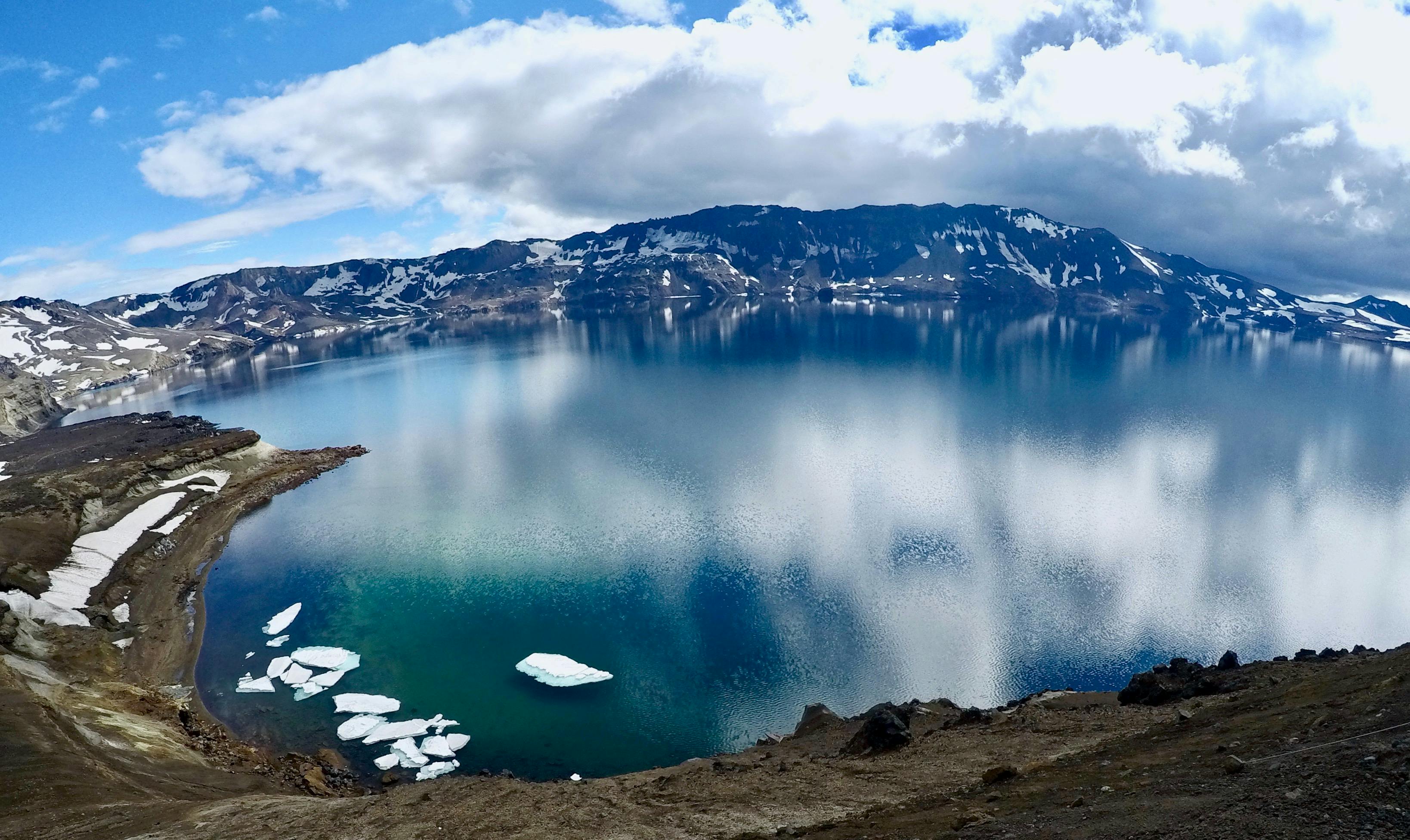 Prescription Goggle Inserts - Breathtaking aerial view of an Icelandic lake surrounded by snow-capped mountains, reflecting the cloudy sky.