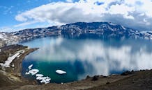 从空中俯瞰，冰岛湖泊令人惊叹，四周雪山环绕，倒映着多云的天空