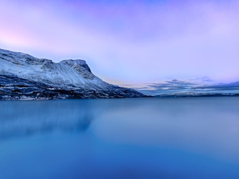 Stunning winter view of a tranquil lake and snow-covered mountains at dawn in Lapland, Finland.