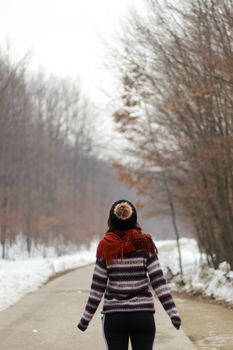 一名妇女穿着温暖的冬季服装，沿着白雪皑皑的森林小路行走