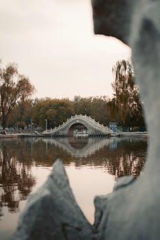 在秋季的公园里，一座传统中式桥梁倒映在宁静的湖面上