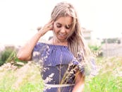 金发女子站在阳光明媚的草地上，低头微笑着