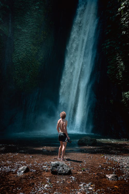 Photo of Man Standing on Rocks Near Waterfalls