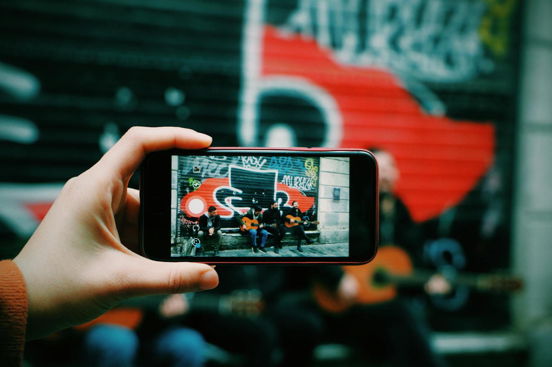 Street musicians playing guitar captured through a smartphone camera in an urban setting.