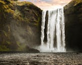 在充满活力的日出下，一个孤独的人欣赏着冰岛令人惊叹的斯科加福斯瀑布