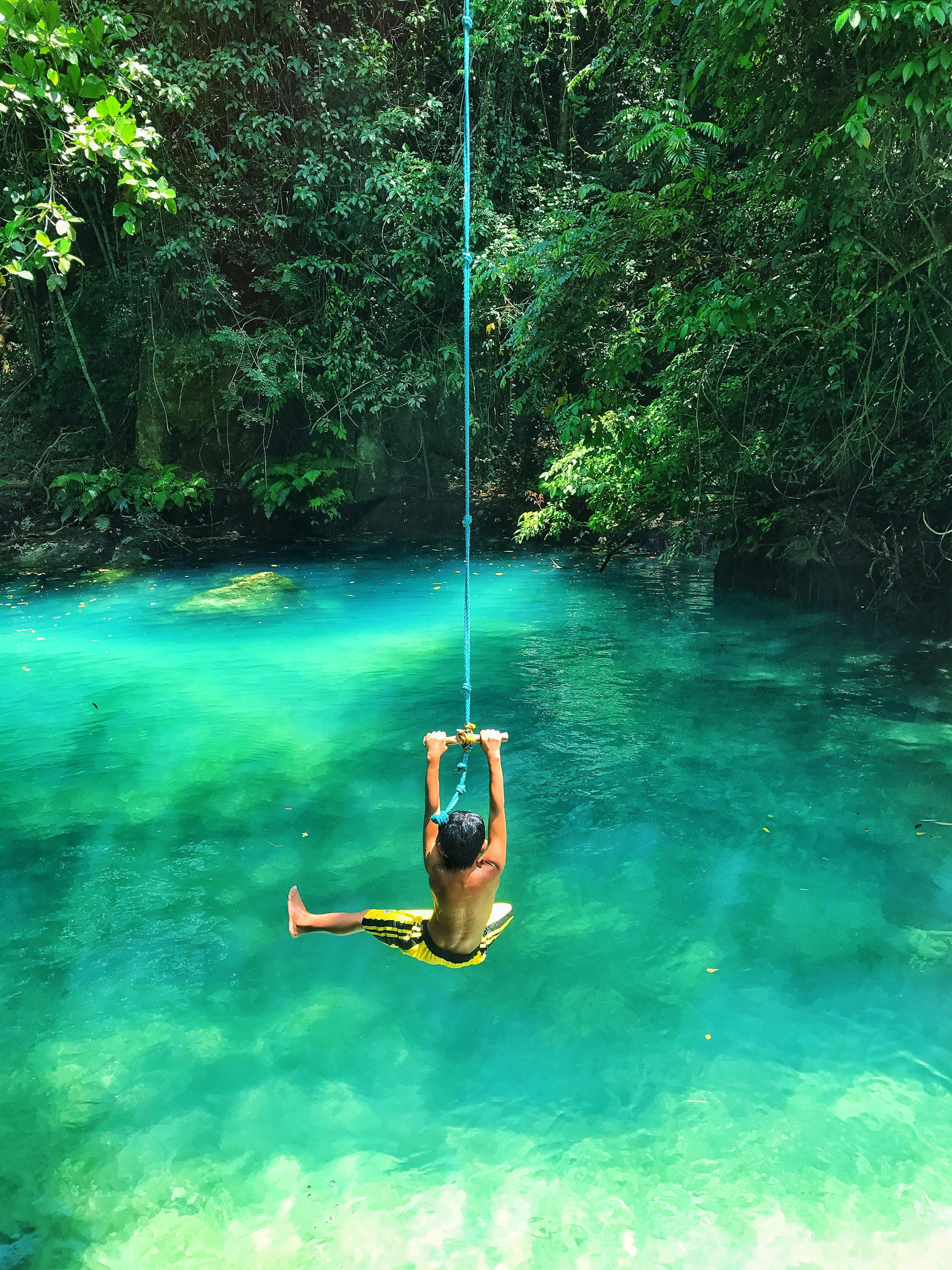 photo of boy swinging over body of water