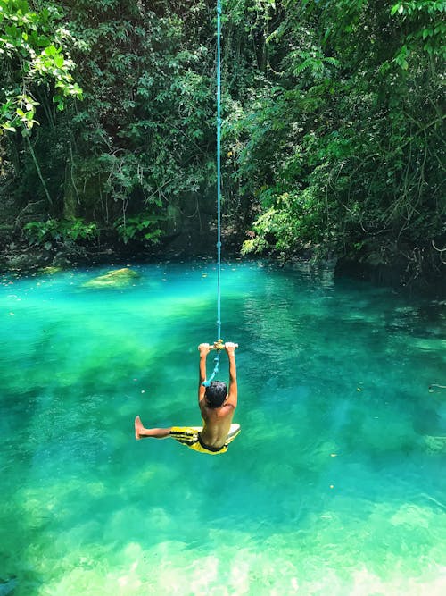 Photo of Boy Swinging Over Body of Water