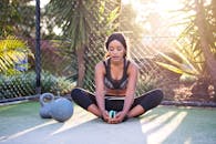 在阳光明媚的日子里，一位女士拿着壶铃练习户外瑜伽和健身，展现了积极的生活方式