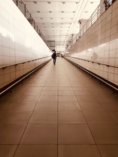 Free A lone person walks down a modern, well-lit hallway with tiled floors and white walls. Stock Photo