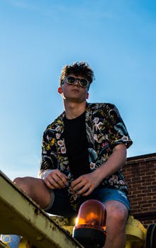 一位戴着太阳镜、穿着花卉衬衫的时尚年轻人，在晴朗的天空下于户外摆姿势