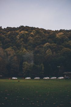 一辆汽车停在秋季的绿色原野和森林山坡旁，构成一幅宁静的场景