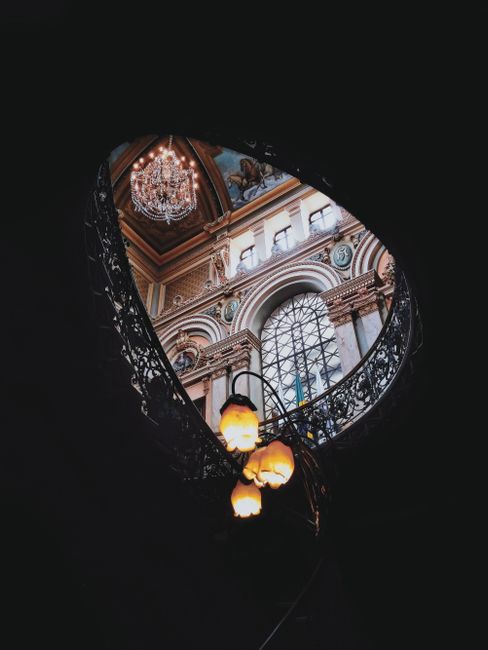 Elegant gothic architecture with stained glass and chandelier viewed through an arch.