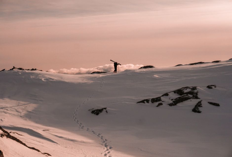 A lone skier walks across a snow-covered mountain at dusk, creating a sense of adventure and solitude.