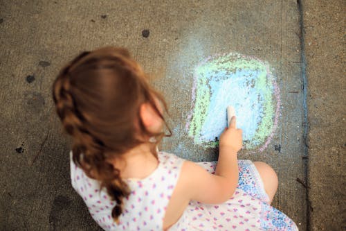 Kleines Mädchen, Das Auf Pflaster Mit Farbiger Kreide Zeichnet