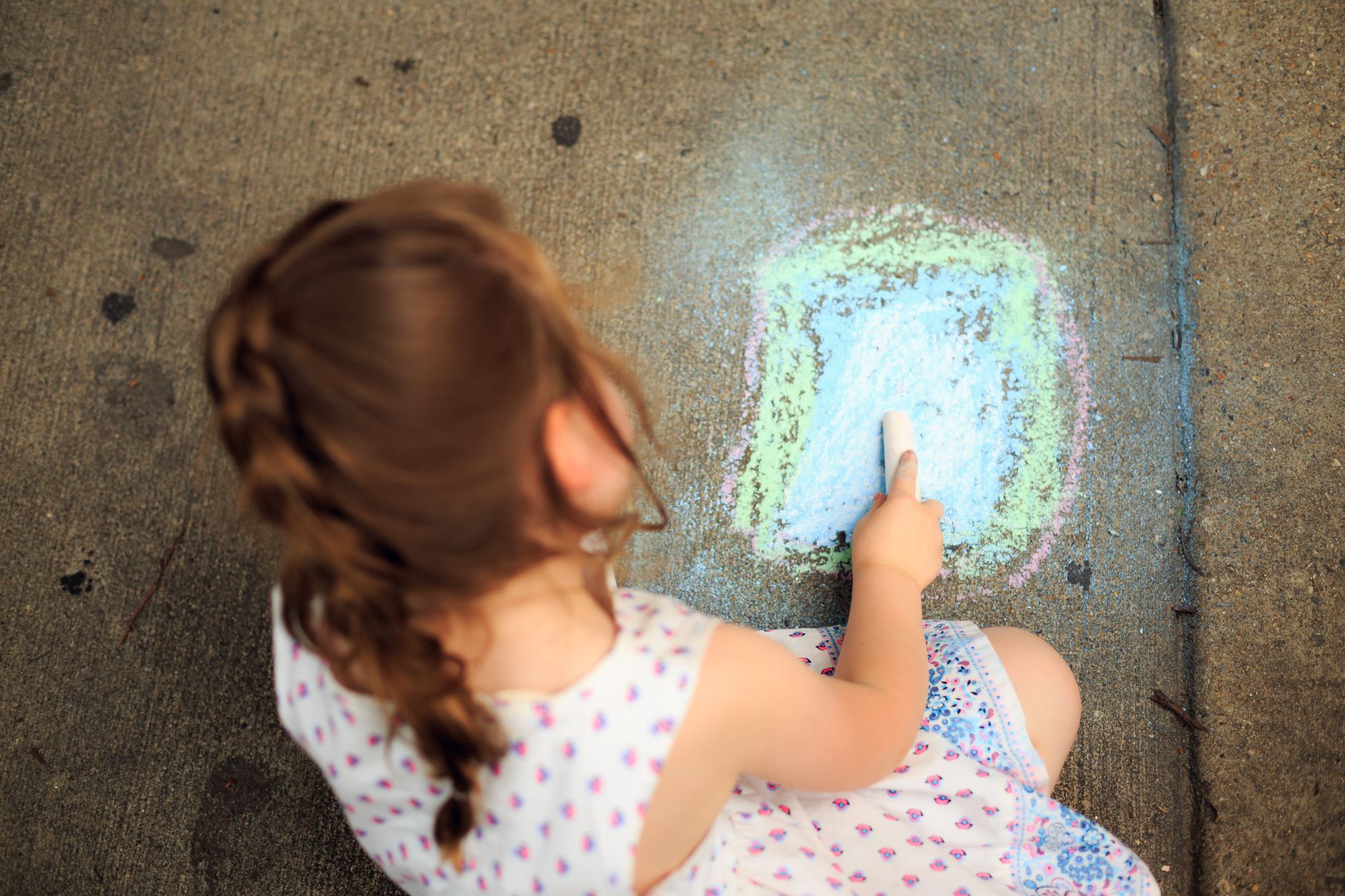 A young girl creatively drawing on the sidewalk with colorful chalk, capturing a moment of childhood creativity.