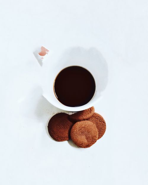 Free Flat lay of a cup of black coffee accompanied by cookies on a stark white background. Stock Photo