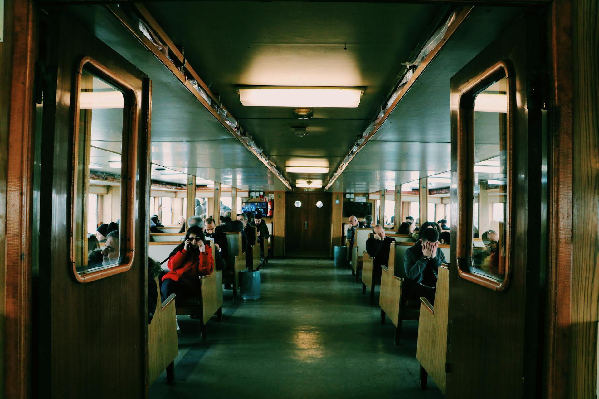 Passengers seated inside a modern ferry with wooden interiors and large windows, reflecting urban travel.