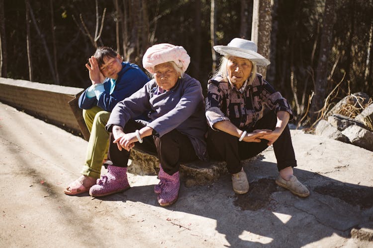 Three People Sitting Beside Pavement