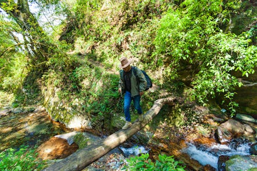 Uomo In Camicia Nera, Giacca Verde E Jeans Blu Che Attraversano La Passerella Sul Torrente