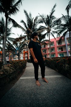 A man walking barefoot on a palm-lined path in Puerto Vallarta, with vibrant buildings and lush greenery.