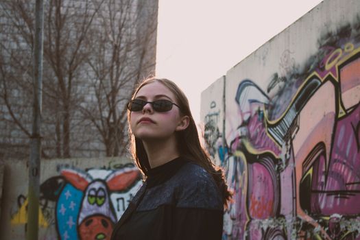 Stylish woman in sunglasses posing against colorful graffiti wall, showcasing urban street art.
