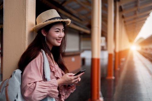 A smiling traveller with a backpack and a phone at a station.