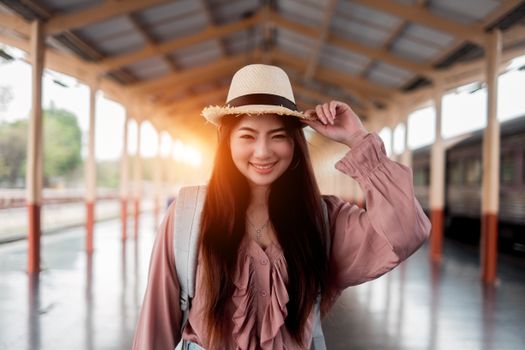 Happy woman with long hair and straw hat posing at a sunny train station.
