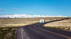 房车沿着蜿蜒的道路行驶，背景是白雪皑皑的壮丽山脉