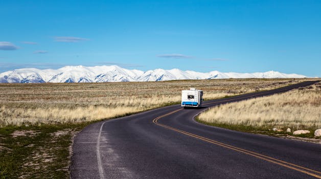 房车沿着蜿蜒的道路行驶，背景是白雪皑皑的壮丽山脉