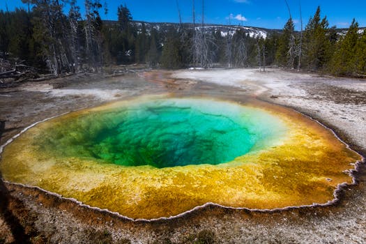 A colorful and steaming hot spring in Yellowstone National Park surrounded by stunning natural scenery.