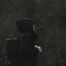 一名身穿连帽衫、背着背包的男子，在黑暗的自然环境中侧身而立，与世隔绝