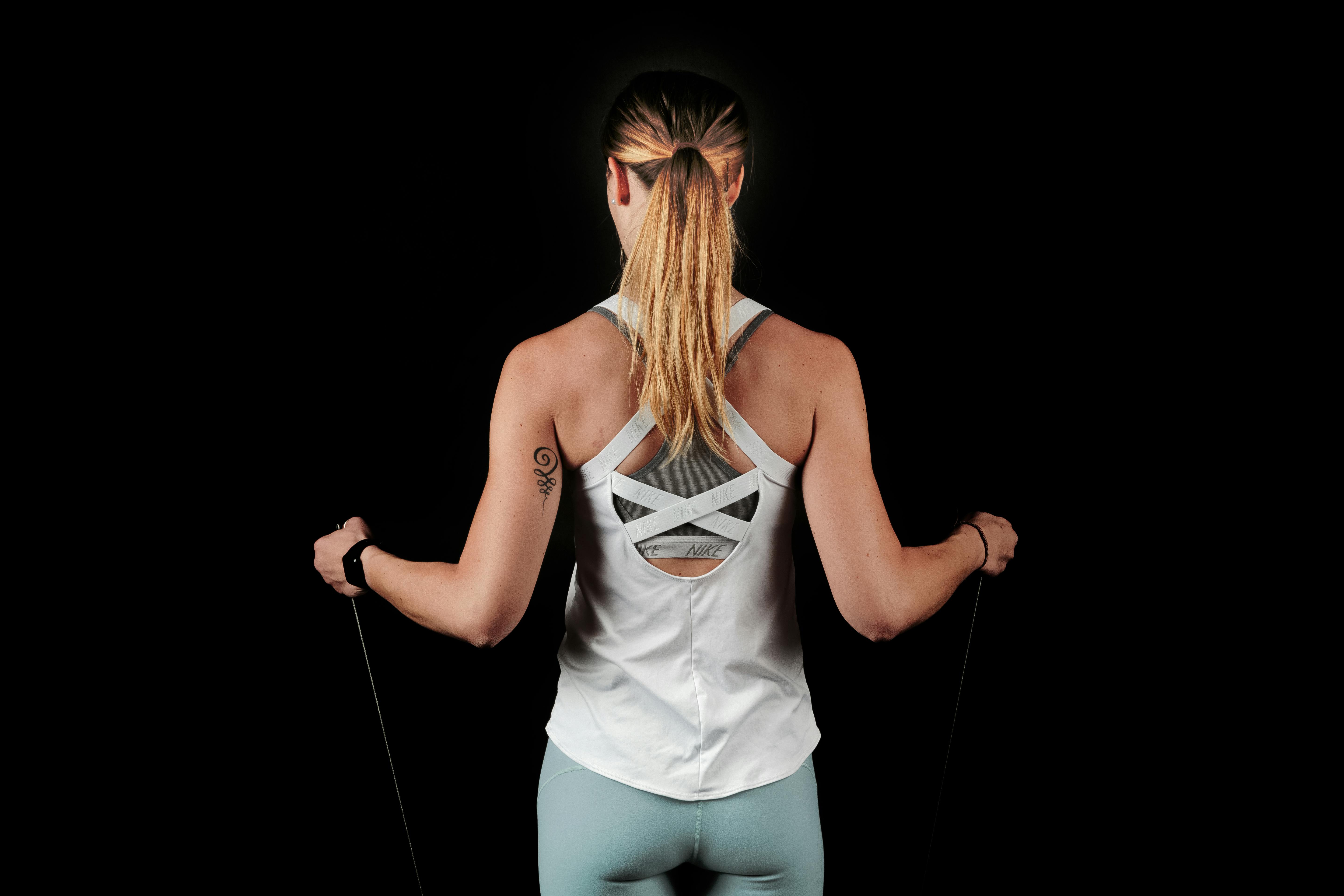 女人站在黑色背景上时拉着她的手臂的抵抗带的背影照片 免费素材图片
