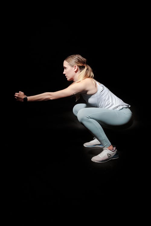Side View Photo of Woman Doing Squats Against Black Background