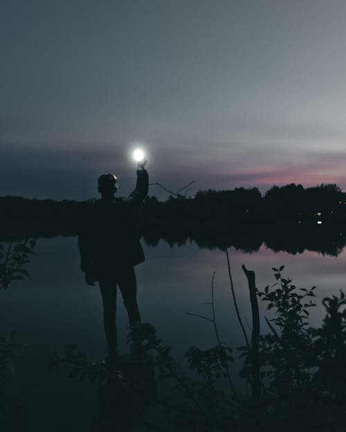 Free Silhouette of Person Standing Near Body of Water Stock Photo