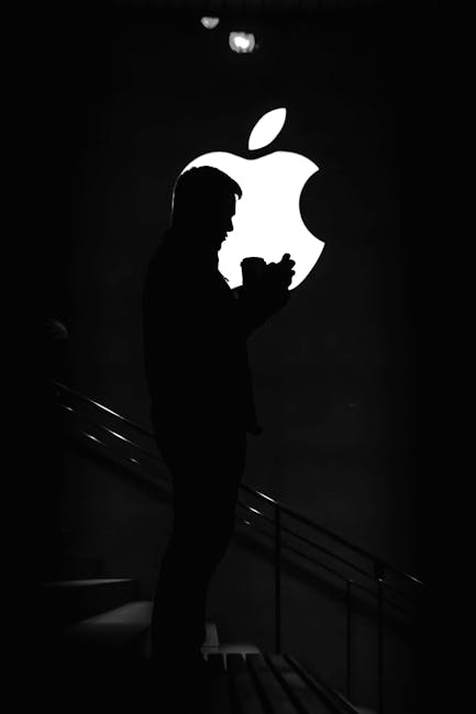 Silhouetted man against bright Apple logo, creating dramatic contrast.
