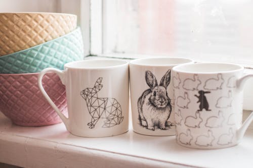Free Three Assorted-design Ceramic Mugs next to a Pile of Ceramic Bowls Stock Photo