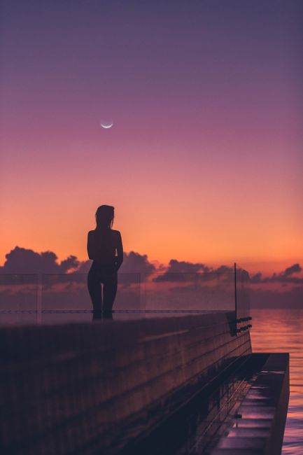 A mesmerizing twilight scene with a silhouetted woman on a Maldives pier under a crescent moon.