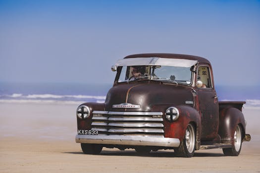 Classic Chevrolet pickup truck driving on a sandy beach with ocean view.