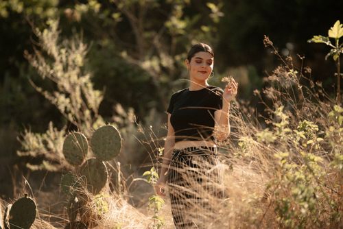Free A woman stands surrounded by cacti and dry grass in a sunlit meadow, exuding joy and calmness. Stock Photo