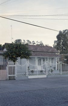 Tranquil suburban scene featuring a classic house behind a white picket fence.