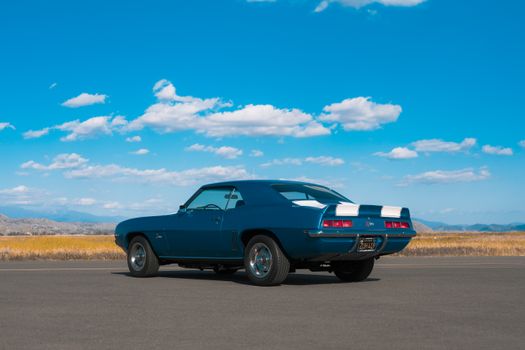 Blue 1969 Chevrolet Camaro parked on asphalt under a clear blue sky.