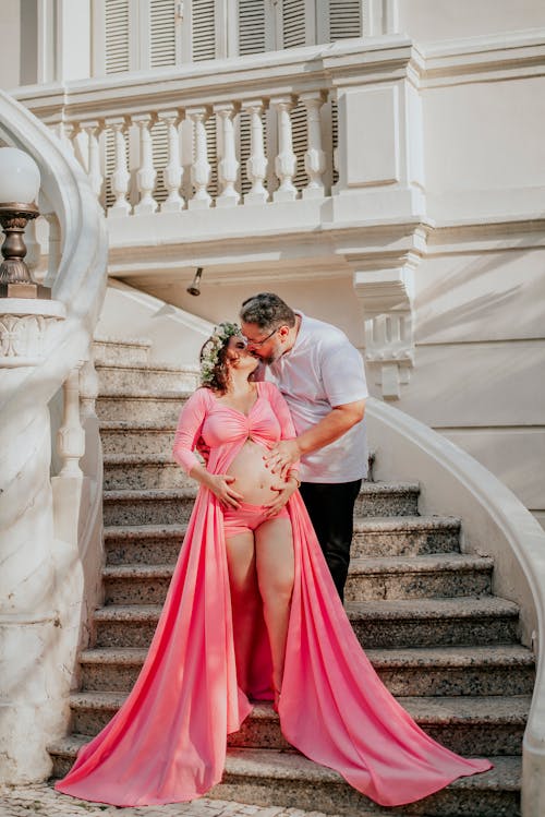 A Man Kissing a Pregnant Woman while Standing on the Stairs