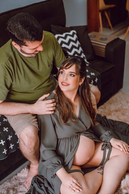 A Pregnant Woman Sitting on the Floor and Her Partner Sitting behind Her on a Couch 