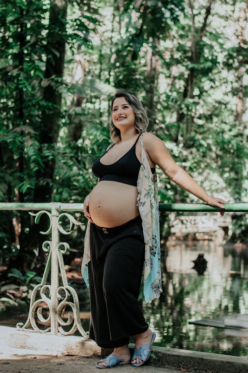 A Pregnant Woman Standing on a Bridge in a Park 