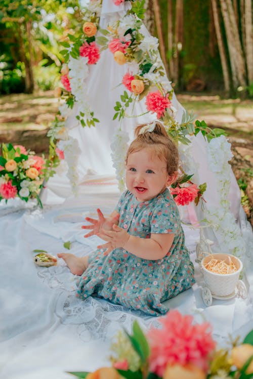 A baby girl sitting on the ground in front of a table with flowers and fruit