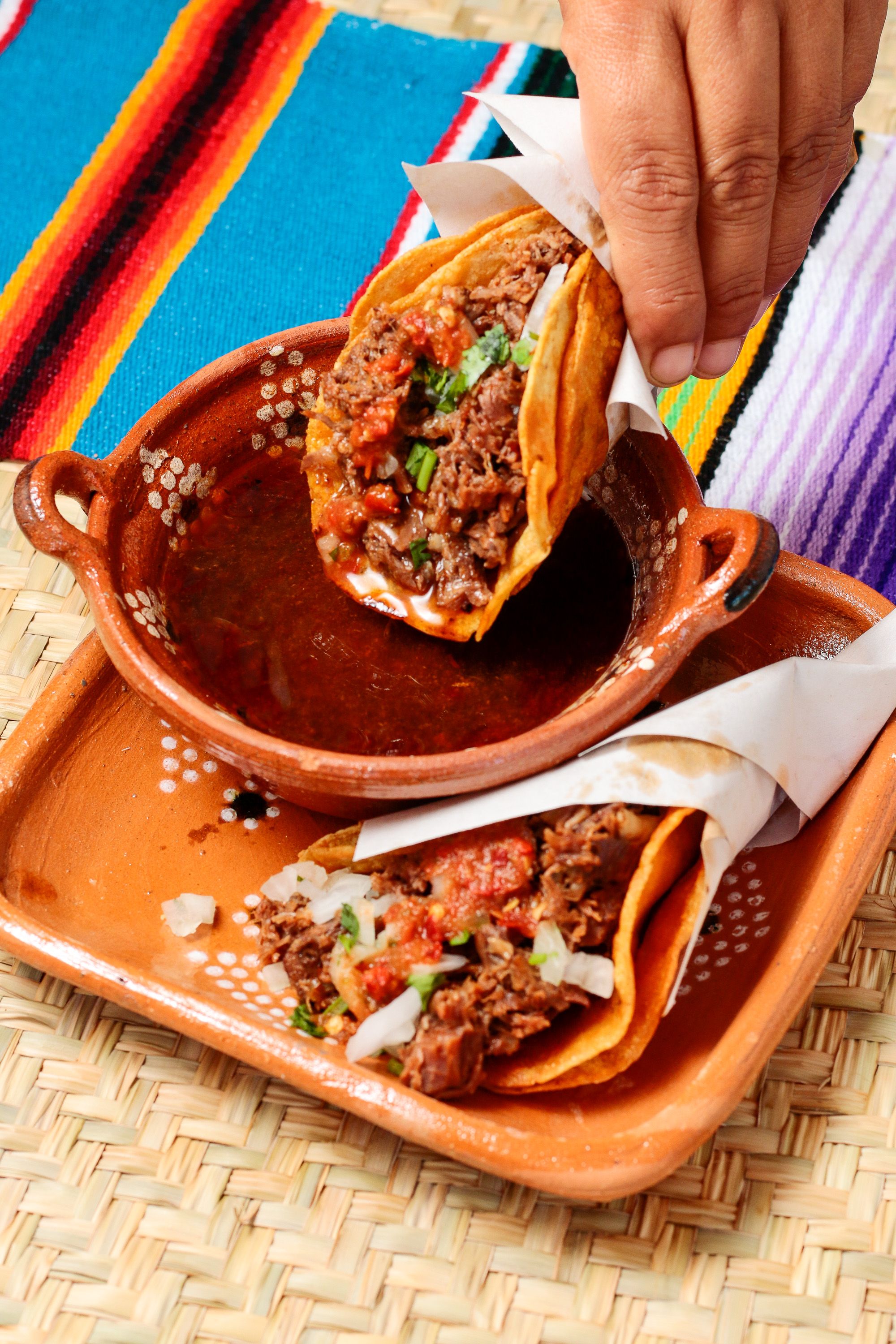 A spread of SHRK's Birria Tacos with consomé dipping bowls, showcasing the rich colors and textures of authentic birria preparation
