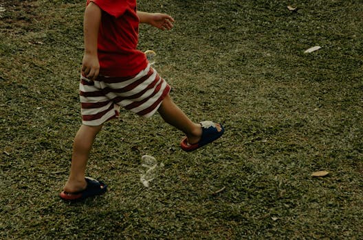 Young child walking on grass with red striped shorts and flip flops outdoors