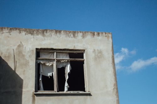 Free A decaying building facade showcasing a broken window against a clear blue sky. Ideal for urban exploration themes. Stock Photo