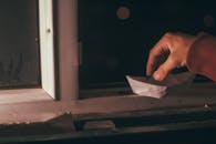 一只手将一艘纸船放在窗边，捕捉了夜晚充满创意与怀旧的瞬间